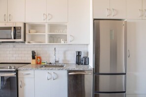A modern kitchen with white cabinets, a stainless steel refrigerator, a microwave, and a coffee maker. - Luxury Penthouse Apt Near Brady St with Balcony and Lake View (Milwaukee)