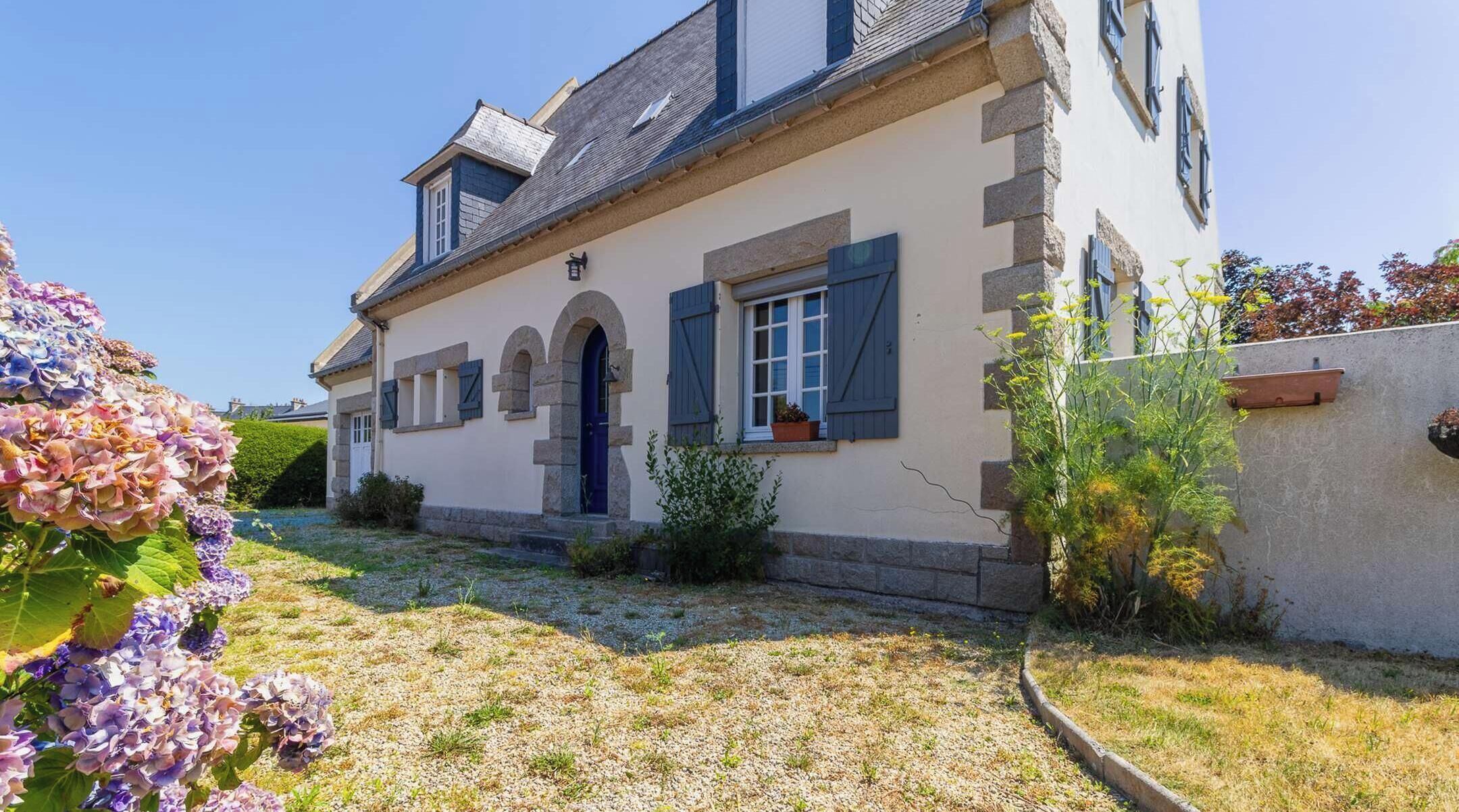 A house with a stone facade, a blue door, and a small garden with hydrangeas.