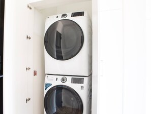 A stacked washer and dryer unit in a white-walled room with a door. - Luxury Penthouse Apt Near Brady St with Balcony and Lake View (Milwaukee)