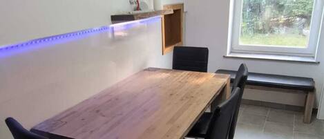 Un comedor moderno con una mesa de madera, sillas negras, un banco, un cuadro enmarcado y un tragaluz.