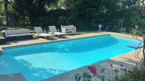 Piscina con sillones de descanso y un banco, rodeada de vegetación.