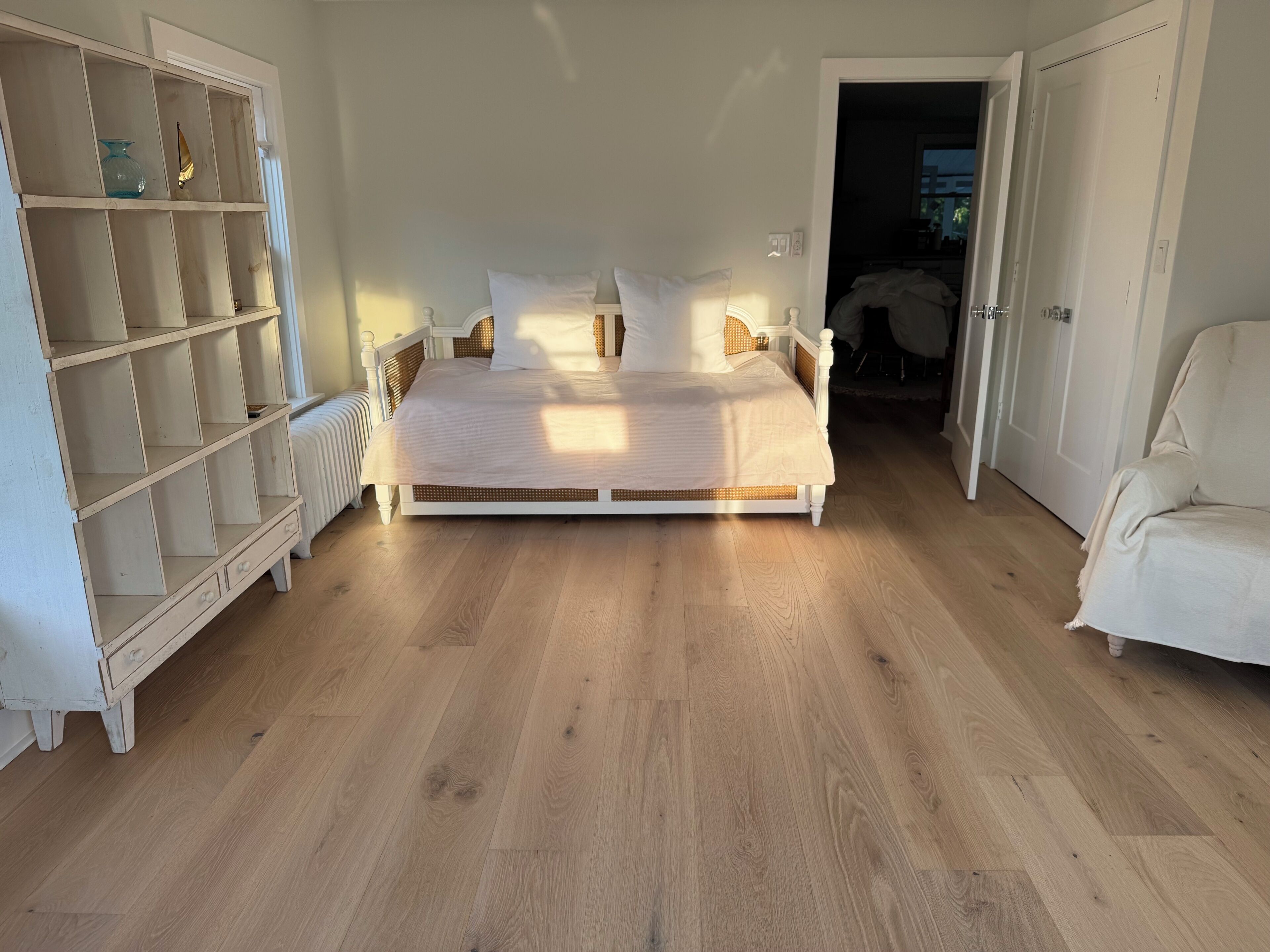 A bedroom with a large bed, a white wardrobe, and a chair.
