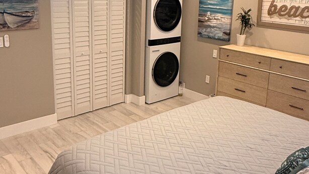 Ein Schlafzimmer mit einem Bett, einem Deckenventilator, einer an der Wand montierten Waschmaschine und einem Trockner, einer Kommode und einem Gemälde.