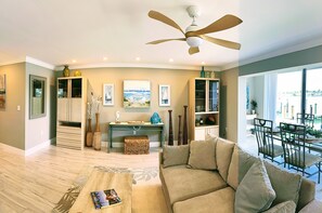 A spacious living area with a ceiling fan, a sofa, a coffee table, and a dining area with chairs. - Beautiful waterfront condo with stunning views of Mooring Bay (Naples)
