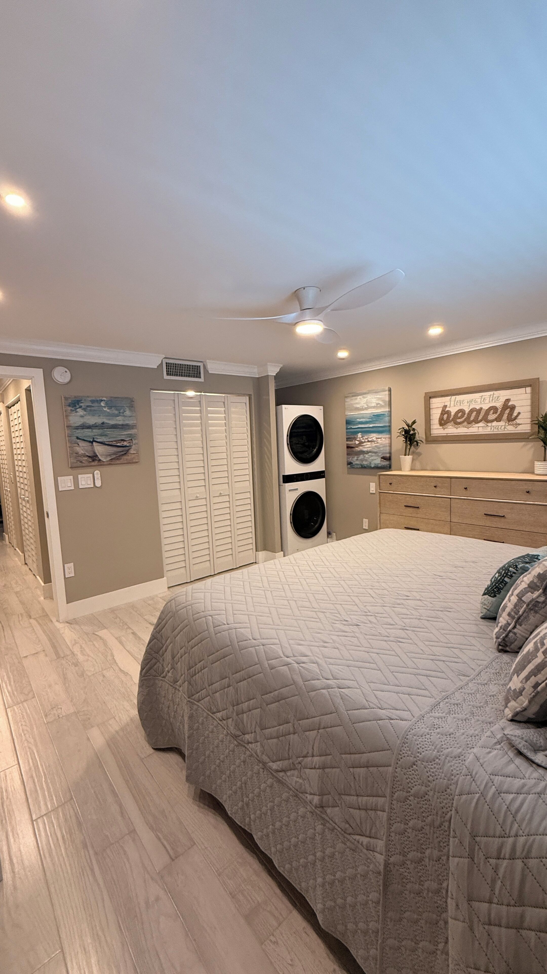 Une chambre avec un lit, un ventilateur de plafond, un lave-linge fixé au mur, un placard et une décoration murale sur le thème de la plage.