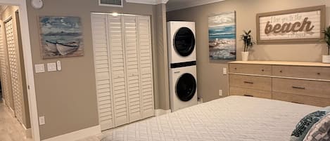 Une chambre avec un lit, un ventilateur de plafond, un lave-linge fixé au mur, un placard et une décoration murale sur le thème de la plage.