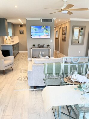A modern living room with a sofa, a glass coffee table, and a television mounted on the wall. - Beautiful waterfront condo with stunning views of Mooring Bay (Naples)
