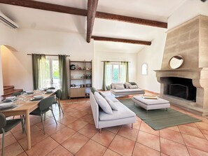 A spacious living area with a fireplace, a dining table set for four, and a sofa. - Villa Océane. Spacious House with Swimming Pool – Pernes-les-Fontaines (Pernes-les-Fontaines)