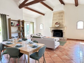 A spacious living area with a fireplace, a dining table set for four, and a sofa. - Villa Océane. Spacious House with Swimming Pool – Pernes-les-Fontaines (Pernes-les-Fontaines)