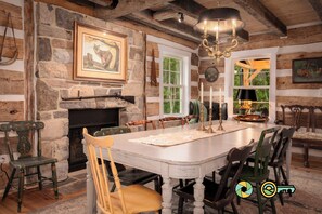 A rustic dining room with a stone fireplace, wooden beams, and a chandelier. - The Sawmill Inn - pre-Civil War luxury log cabin on 70+ private acres! (Mount Jackson)