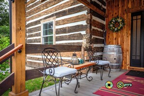 A log cabin with a wooden deck, metal chairs, a table, a barrel, and a wreath on the door. - The Sawmill Inn - pre-Civil War luxury log cabin on 70+ private acres! (Mount Jackson)