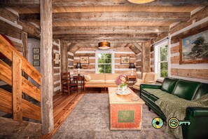 A log cabin interior with a sofa, a green couch, a wooden coffee table, and a staircase. - The Sawmill Inn - pre-Civil War luxury log cabin on 70+ private acres! (Mount Jackson)