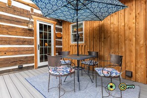 An outdoor patio with a wooden deck, a table with four chairs, and a patterned umbrella.