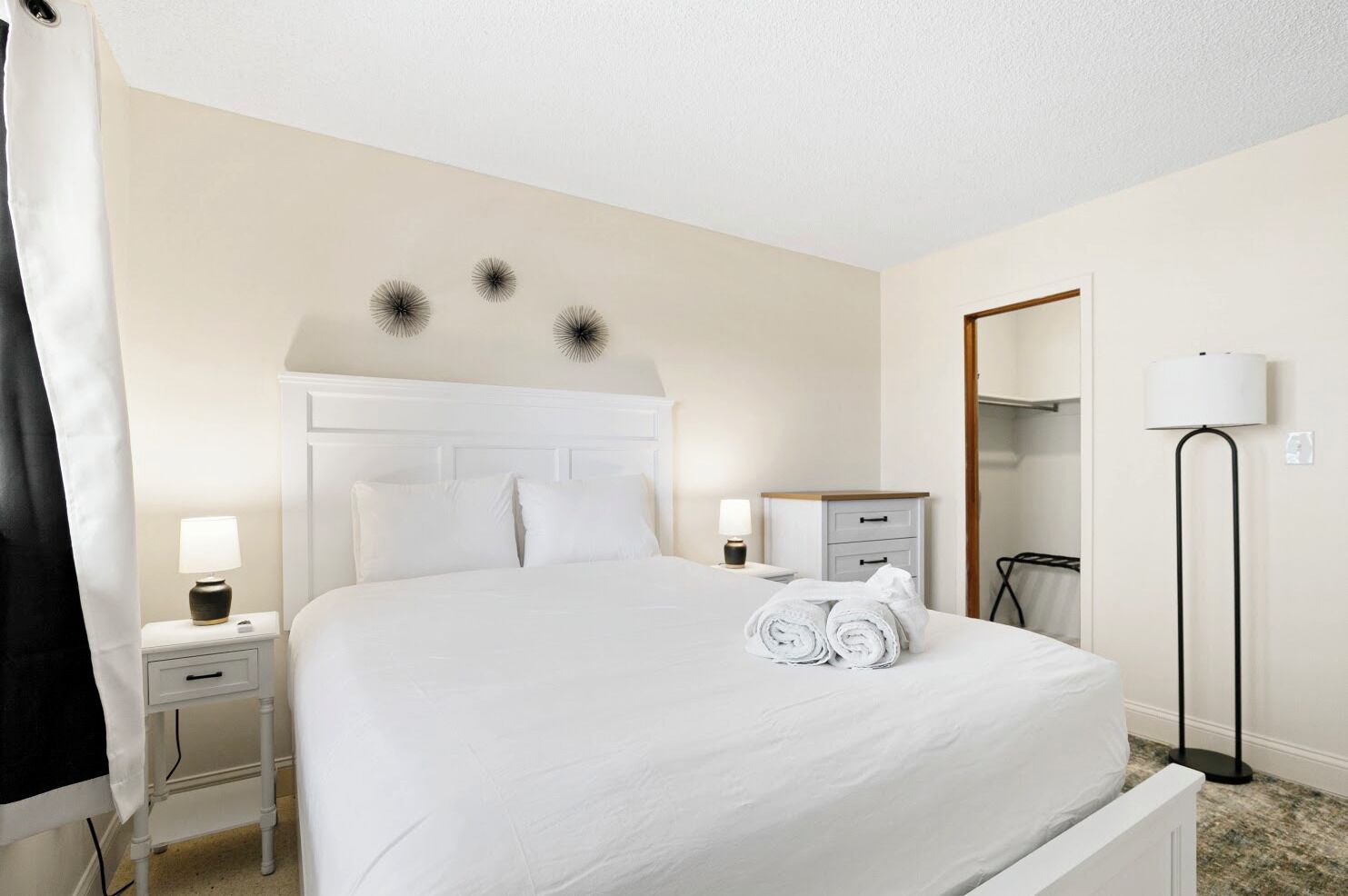 Une chambre d’hôtel avec un grand lit, une table de chevet avec une lampe, une commode, une armoire et un lampadaire.