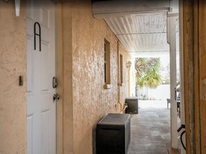 Un garage avec une porte blanche, un sol en béton et un espace abrité avec un banc.