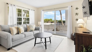 A living room with a grey sofa, a round coffee table, and a TV mounted on the wall. - Snyder's Rest - A managed by Beach Retreats FL (Bradenton Beach)