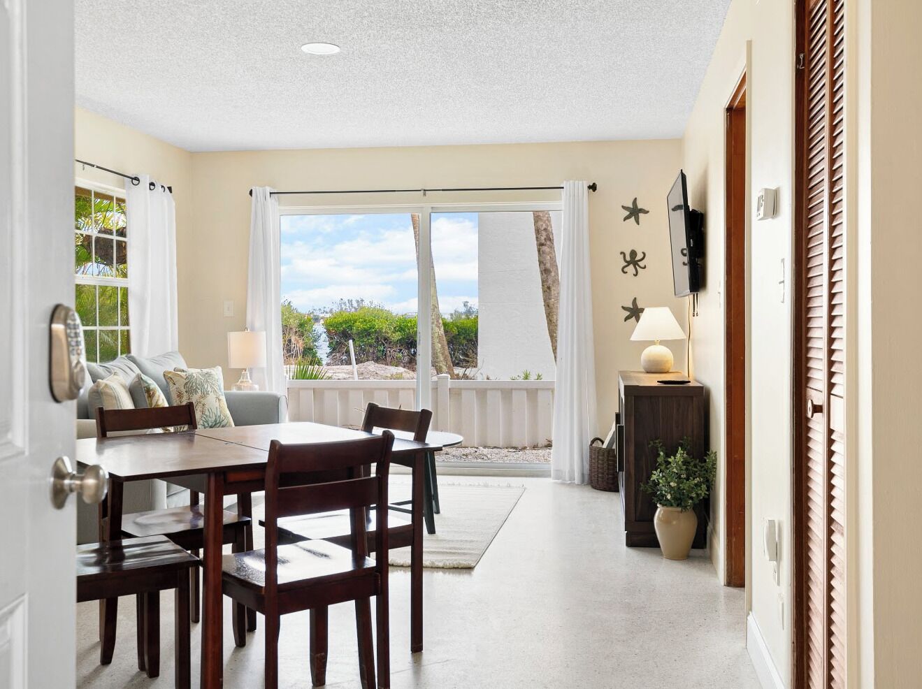 A dining area with a table and chairs, a sofa, a TV, and a view of the outdoors.