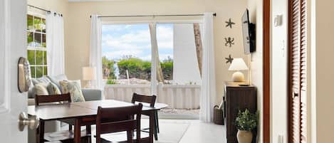 A dining area with a table and chairs, a sofa, a TV, and a view of the outdoors.