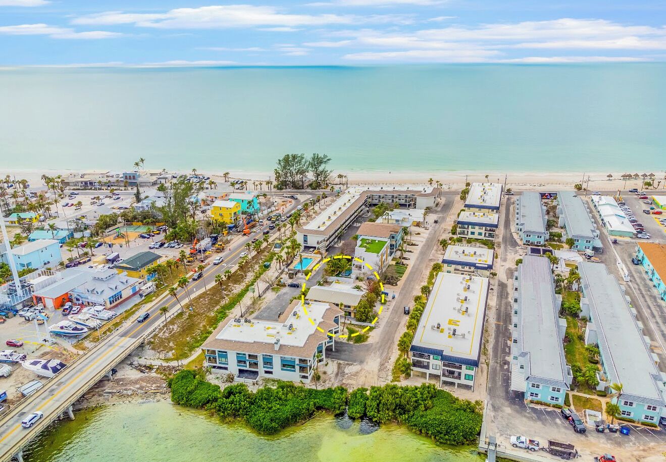 An aerial view of a coastal area with buildings, a beach, and a marina.