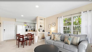 A living room with a grey sofa, a round black table, and wooden chairs. There is a kitchen in the background with white cabinets and a white refrigerator. - Snyder's Rest - A managed by Beach Retreats FL (Bradenton Beach)