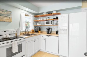 A modern kitchen with white appliances, wooden shelves, and a window with curtains. - Snyder's Rest - B managed by Beach Retreats FL (Bradenton Beach)