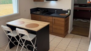 Pieni, käytännöllinen keittiö, jossa on ikkuna, pesuallas, liesi ja pieni ruokailutila tuoleineen.