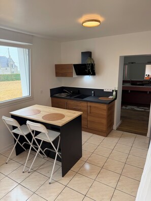 A compact kitchen with a window, a sink, a stove, and a small dining area with chairs. - Brand-new, spacious studio apartment for the 2026 season with a view of the bay (Plouescat)