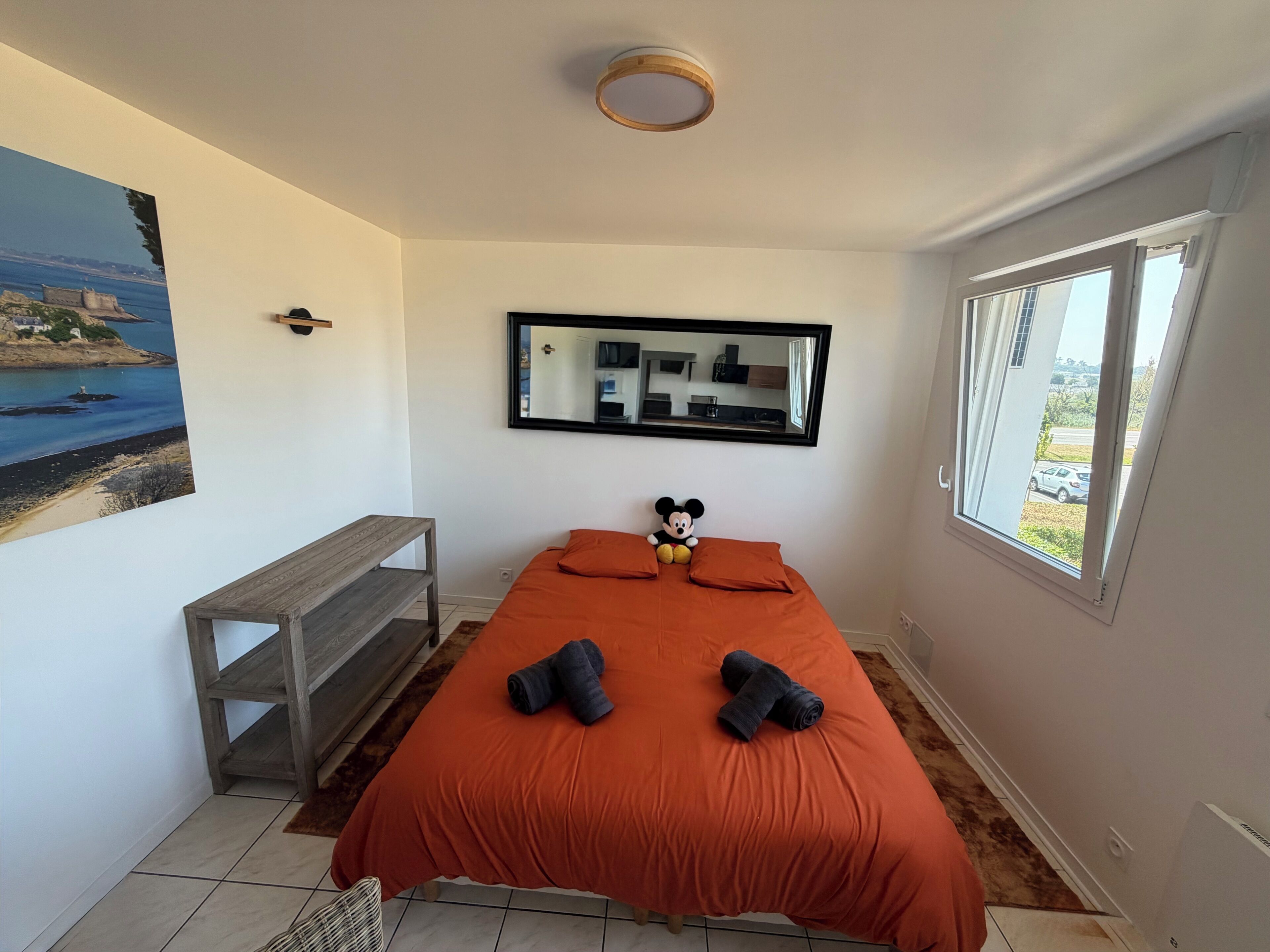 Een slaapkamer met een bed, een bankje, een spiegel en een raam.
