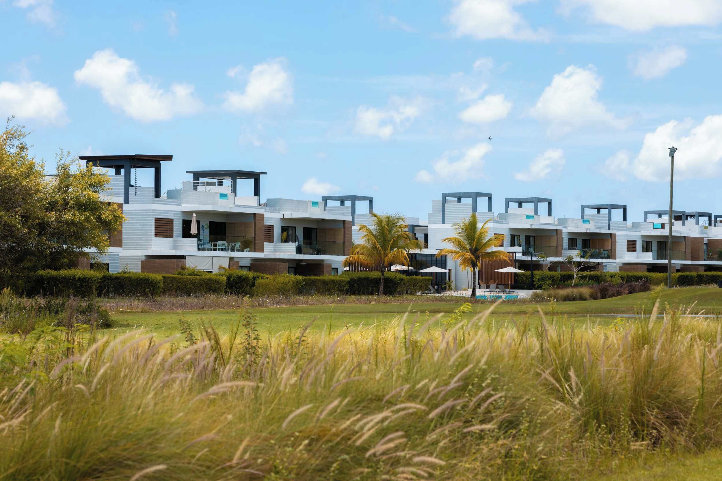 A modern residential complex with multiple levels, outdoor seating areas, and a well-maintained lawn.
