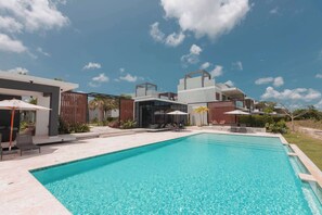 Ein moderner Poolbereich mit klarem, blauem Wasser, Liegestühlen und Sonnenschirmen.