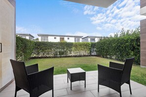 Eine Terrasse mit zwei Korbstühlen und einem kleinen Tisch, ein ordentlich geschnittener Hecke und im Hintergrund der Blick auf moderne Gebäude.
