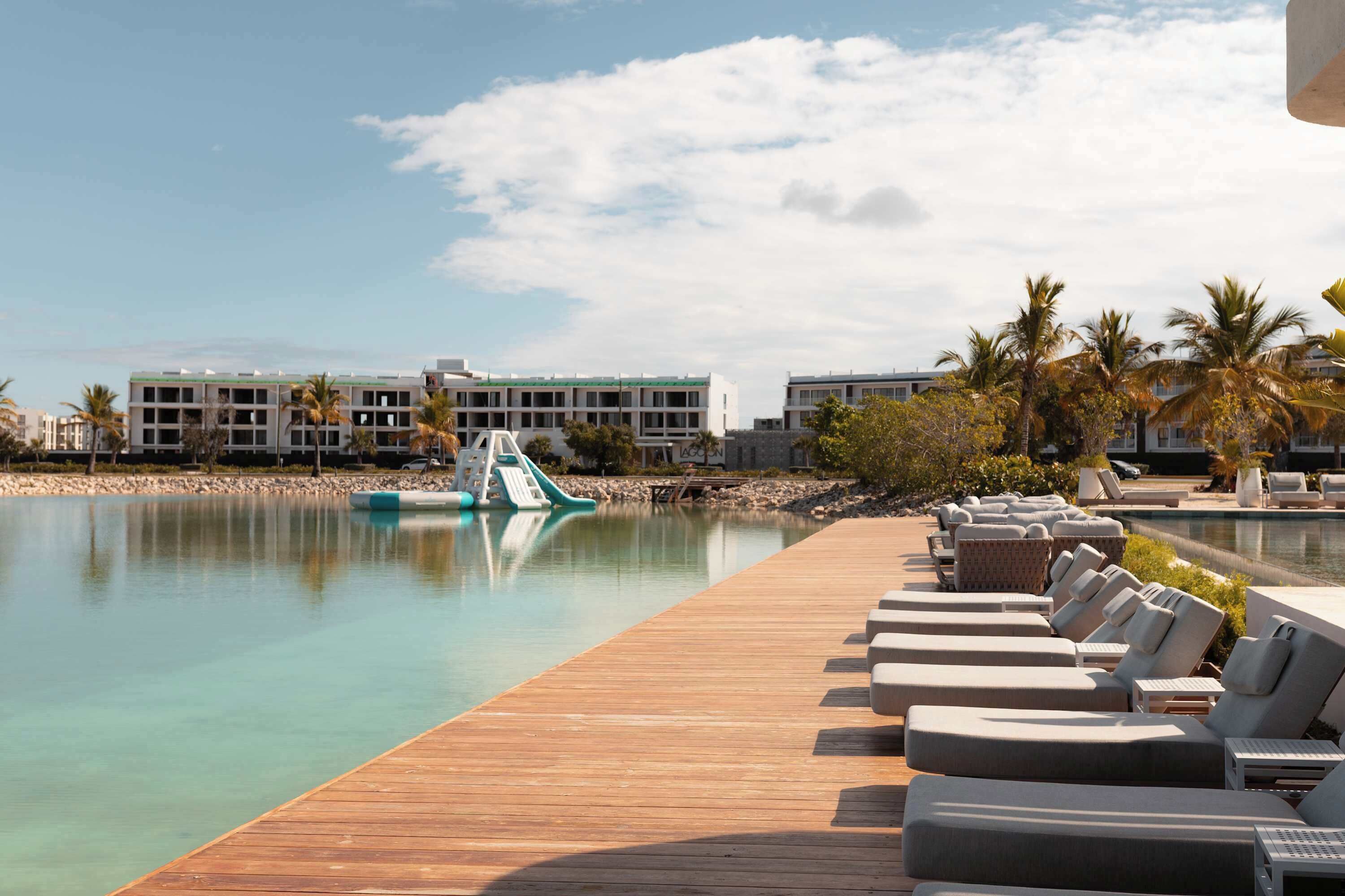 Una piscina de resort con sillas de descanso, una terraza de madera y un edificio al fondo.