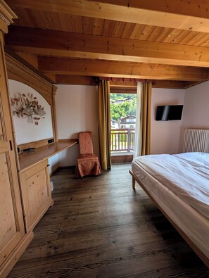 A wooden room with a bed, a chair, a television, and a window with curtains. - Double or Twin Room with Private Bathroom (Mestriago)