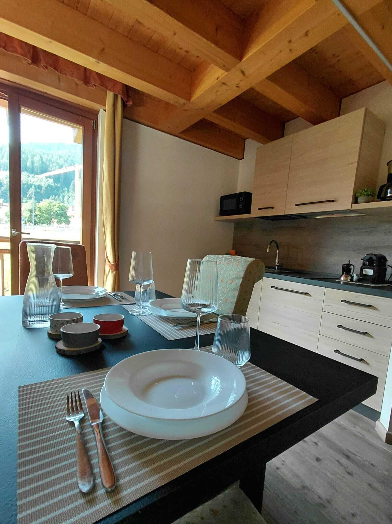 Een eetgedeelte met een tafel voor twee, een keuken met witte kastjes, en uitzicht op de omgeving.