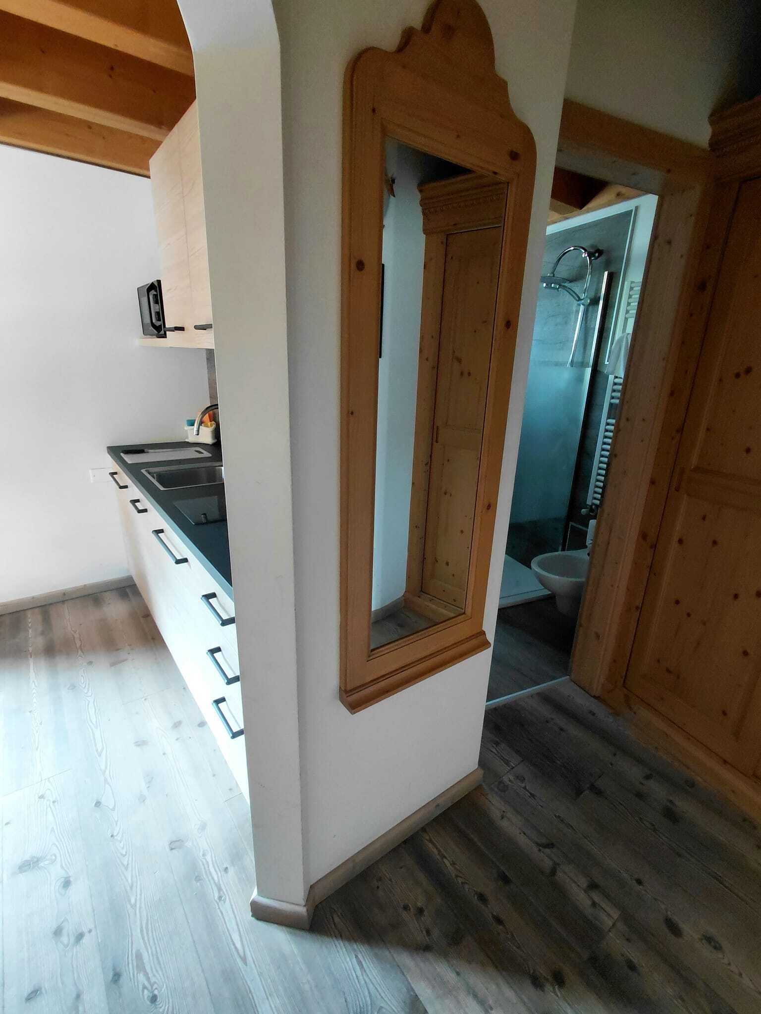 Une pièce avec un miroir encadré en bois, un coin cuisine avec un évier et une vue sur une salle de bain.