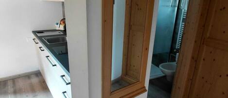 A room with a wooden-framed mirror, a kitchen area with a sink, and a view into a bathroom.