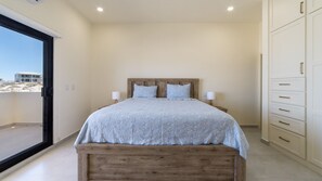 Ein Schlafzimmer mit Bett, Nachttischlampen, einem Holz-Kopfteil und Blick ins Freie.