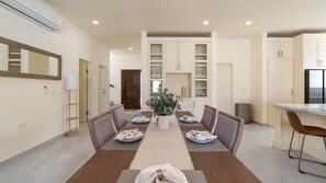 Uma zona de refeições moderna com uma mesa central, cadeiras e um vaso de plantas.