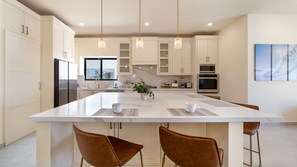 Une cuisine moderne dotée d’un grand îlot central, d’appareils électroménagers en acier inoxydable et de luminaires suspendus.