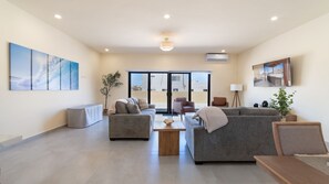 A modern living room with a sofa set, a coffee table, and a side table. There is a large window with a view of buildings outside. - Casa Rubi  5 bedroom home in the beachfront (Puerto Peñasco)