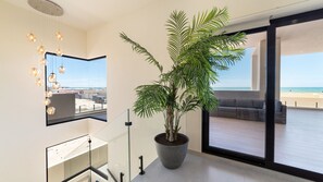 Ein modernes Wohnzimmer mit einer großen Pflanze im Topf, einer Glastrennwand und Blick auf den Strand.