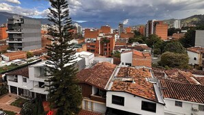 A residential area with a mix of modern and traditional architecture, including a prominent pine tree and a parking lot with cars. - Duplex With Incredible View Rooftop Jacuzzi & GYM (Medellín)