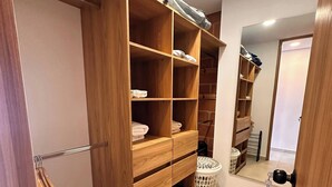 A wooden closet with multiple shelves and hanging space, a laundry basket, and a door with a key lock. - Duplex With Incredible View Rooftop Jacuzzi & GYM (Medellín)