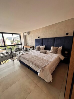 Ein modernes Schlafzimmer mit einem großen Bett, einem kleinen Tisch und einem Balkon mit Blick auf Gebäude.