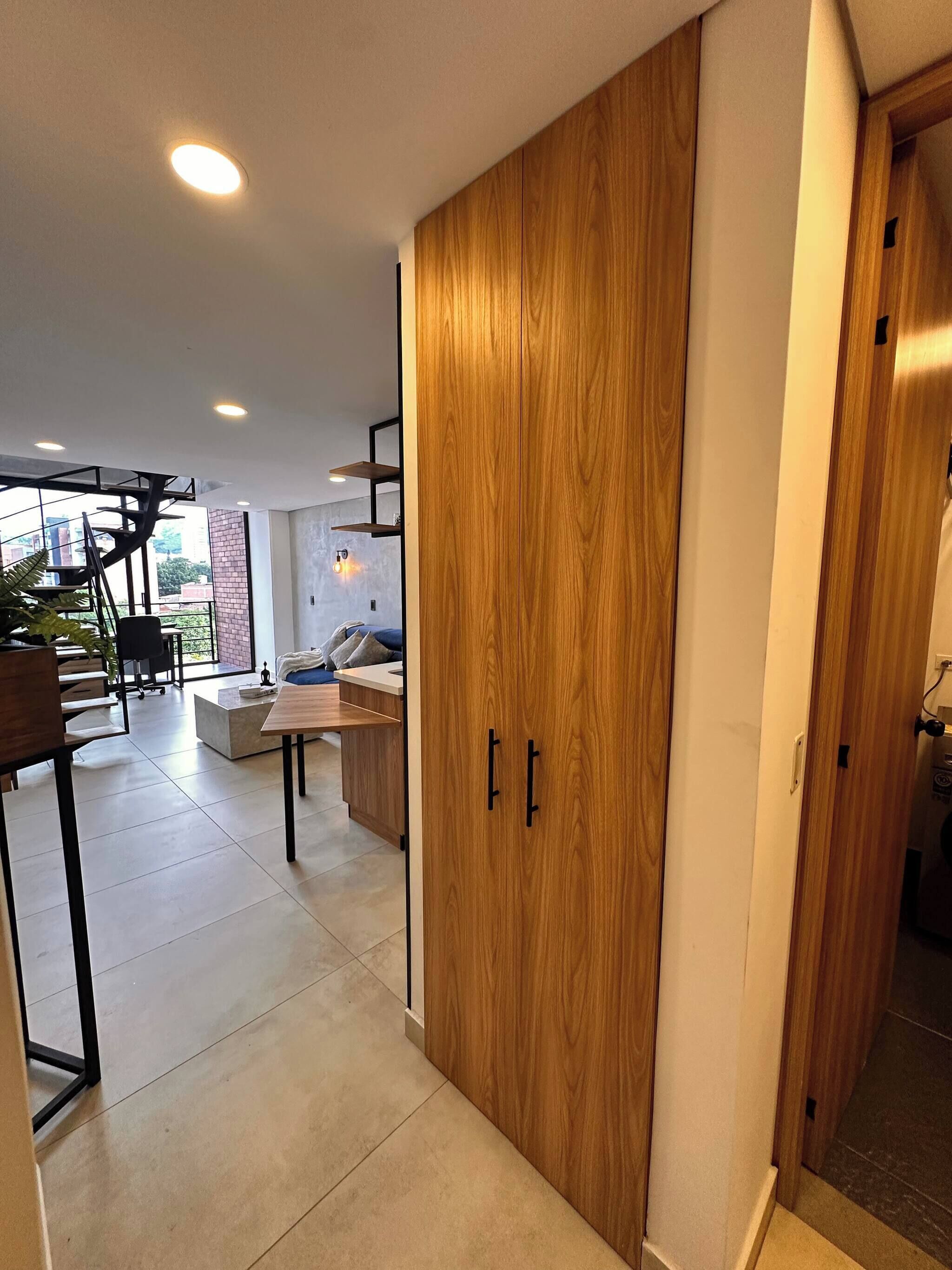 A modern interior with a wooden wardrobe, a dining area with a table and chairs, and a kitchen area with a countertop and cabinets.