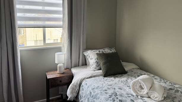 Une chambre à coucher avec un lit, une table de chevet, une lampe et une fenêtre avec des rideaux.