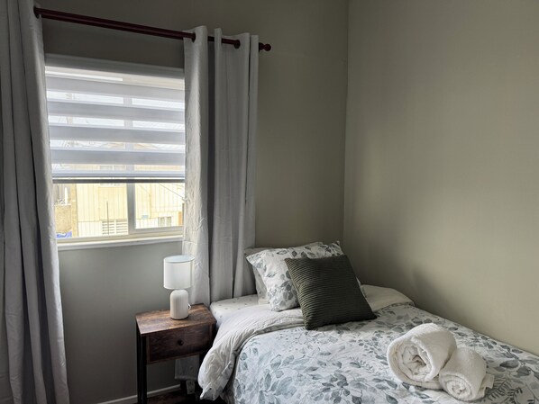A bedroom with a bed, a nightstand, a lamp, and a window with curtains.