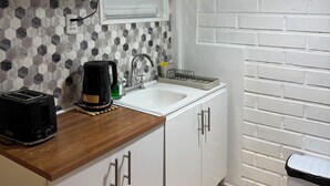 Une cuisine avec des meubles blancs, un pare-feu en carreaux, un évier, un grille-pain, une bouilloire et un luminaire suspendu.