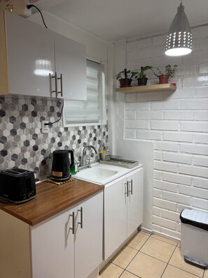 A kitchen with white cabinets, a tiled backsplash, a sink, a toaster, a kettle, and a hanging light fixture.