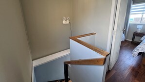 Une pièce avec un escalier, un plancher en bois, un mur blanc et une fenêtre avec des rideaux.